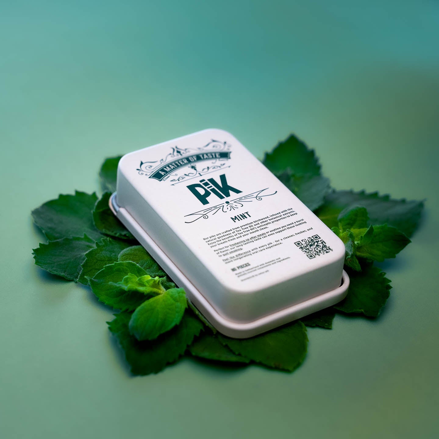 High-resolution image of Pik Mint flavored toothpicks tin back label, highlighting ingredients, certifications, and product info. Set on peppermint leaves to emphasize freshness and natural origin.