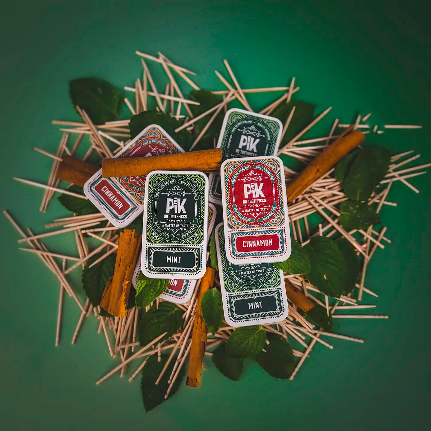 Image of a 6-pack of Pik Mint flavored toothpicks, arranged with fresh mint leaves to highlight the product’s natural ingredients and refreshing aroma. Showcases the clean design, compact tins, and premium Swiss craftsmanship.