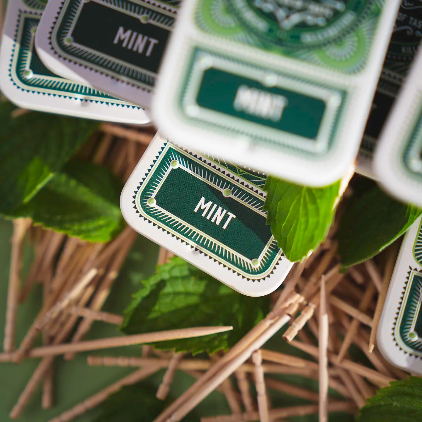 Close-up image of Pik Mint flavored toothpicks, highlighting the intricate design of the recyclable tin, surrounded by fresh peppermint leaves and natural birchwood. Emphasizes the product’s Swiss craftsmanship, eco-conscious packaging, and attention to detail.