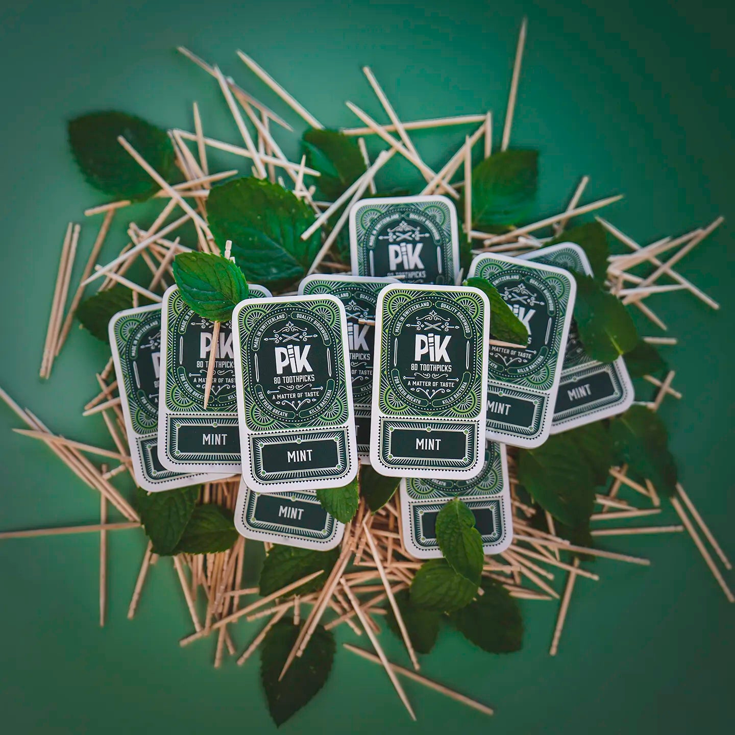 Image of a 10-pack of Pik Mint flavored toothpicks displayed over fresh peppermint leaves. Highlights the eco-conscious, premium design and lasting freshness of this Swiss-made product. Perfect for those who never want to run out of their favorite flavor.