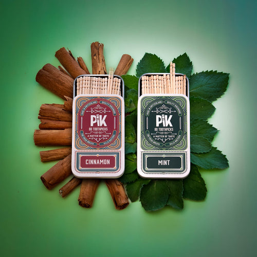 Image of Pik’s Ice & Fire duo featuring two open tins of flavored toothpicks: Cinnamon on a bed of cinnamon sticks and Mint on fresh mint leaves. Highlights the contrasting flavors, elegant packaging, and natural ingredients of this Swiss-made, vegan product.