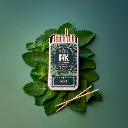 Premium closeup of Pik cinnamon-flavored toothpicks in branded metal tin. Eco-friendly, vegan, and made with certified organic essential oils. Shot on red background with real cinnamon sticks for an intense visual identity.